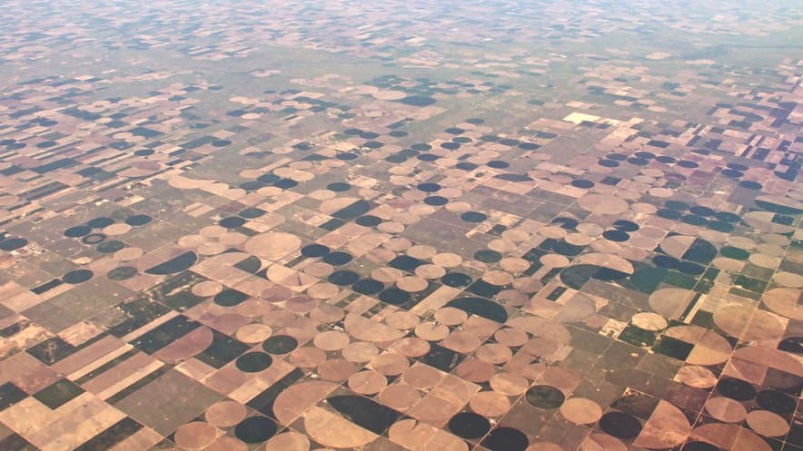 Aerial view of a plain covered to the horizon with hundreds of circular fields watered by center-pivot irrigation.