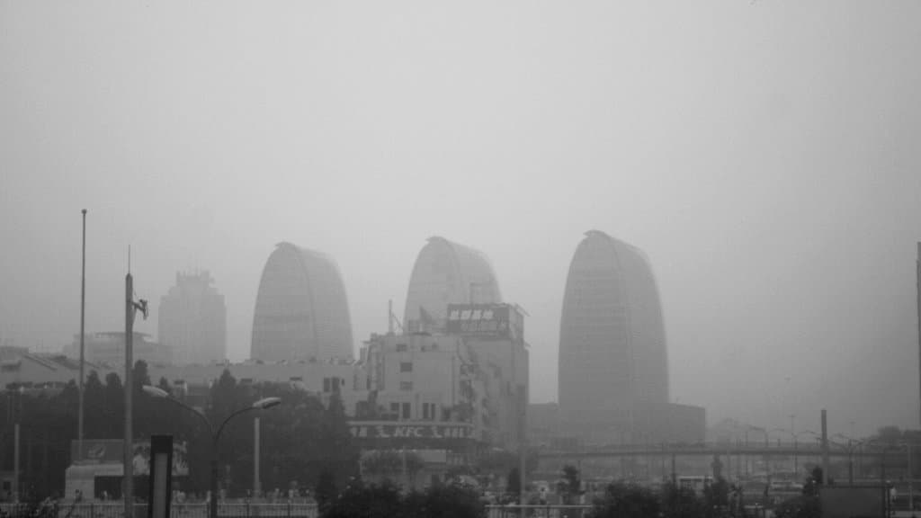 Three curved office towers and lower buildings dissolving into thick gray haze in a Chinese city.