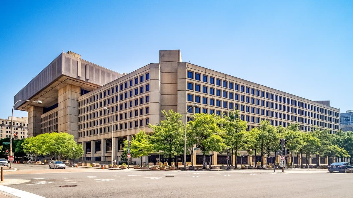 The J. Edgar Hoover Building, a long concrete office block in Washington, seen from a street corner under a clear sky.