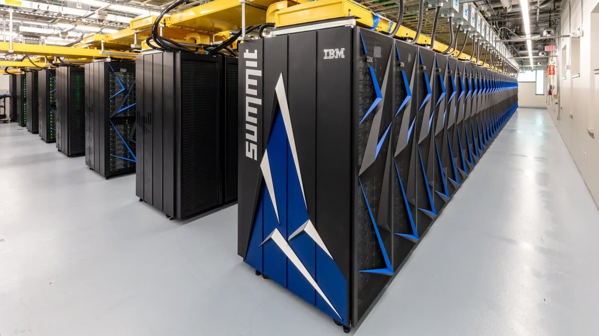 A long row of black computer cabinets in a data center aisle, with yellow cable trays overhead.