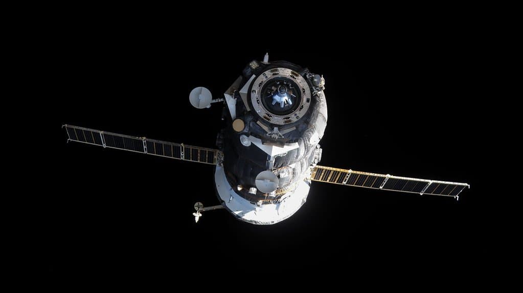A Russian Progress cargo freighter with its two solar arrays extended, photographed in sunlight against black space near the International Space Station.