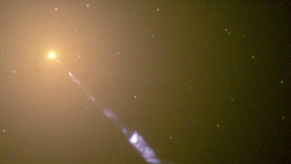 A bright galactic nucleus at upper left with a narrow blue jet of glowing knots streaming diagonally away from it.