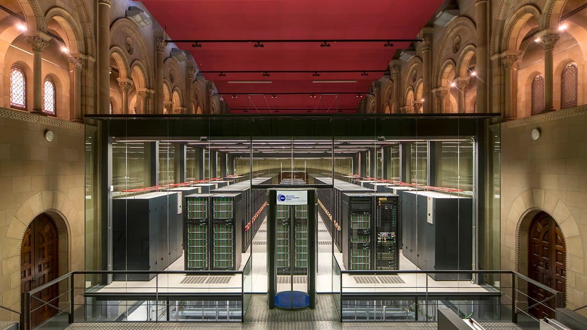 Rows of black computer racks inside a converted stone chapel at the Barcelona Supercomputing Center, seen from a raised walkway.