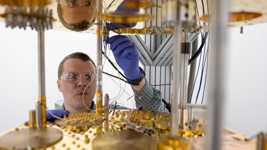 A researcher reaches between the gold-plated cooling stages of a dilution refrigerator to connect wiring inside the cryostat.