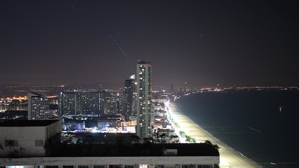 A coastal city at night seen from above, with a brightly lit beachfront strip running along a dark bay.