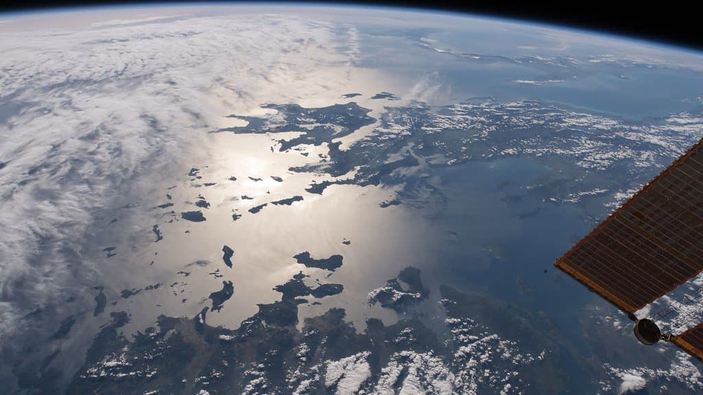 Sunlight glints off the Aegean and Ionian Seas around the Greek islands, photographed from the International Space Station, with a station solar array at the right of the frame.