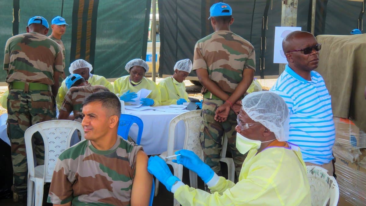 Health workers in yellow gowns, blue gloves and face masks give Ebola vaccinations to seated men at an outdoor vaccination point in Pinga, North Kivu.