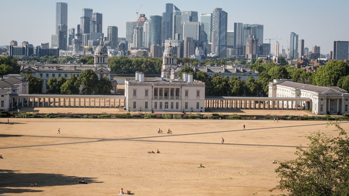 Grass burned brown by heat across a large London park, with the city skyline in the distance.