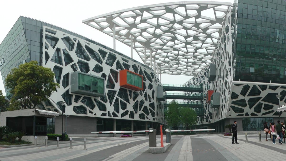The Alibaba Group headquarters building in Hangzhou, China, a glass office block with a white lattice facade and a canopy over the entrance plaza.