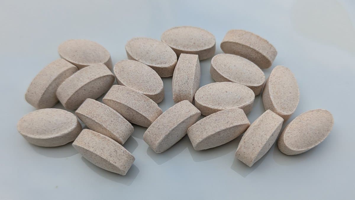 About twenty oval beige vitamin C supplement tablets scattered on a white surface.