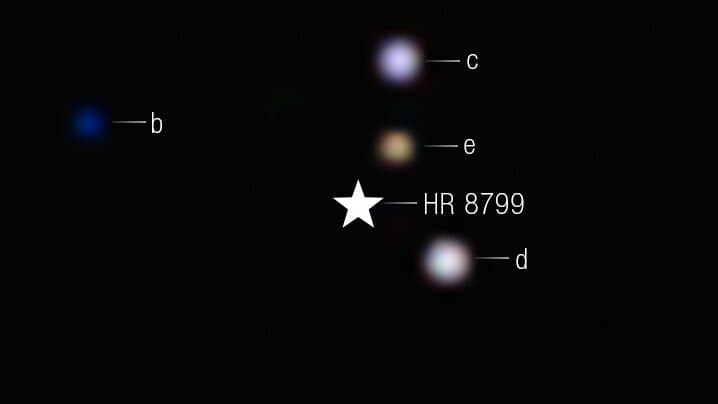 Webb telescope near-infrared image of the star HR 8799, with its four known giant planets labeled b, c, d and e as small colored points of light around the masked star.