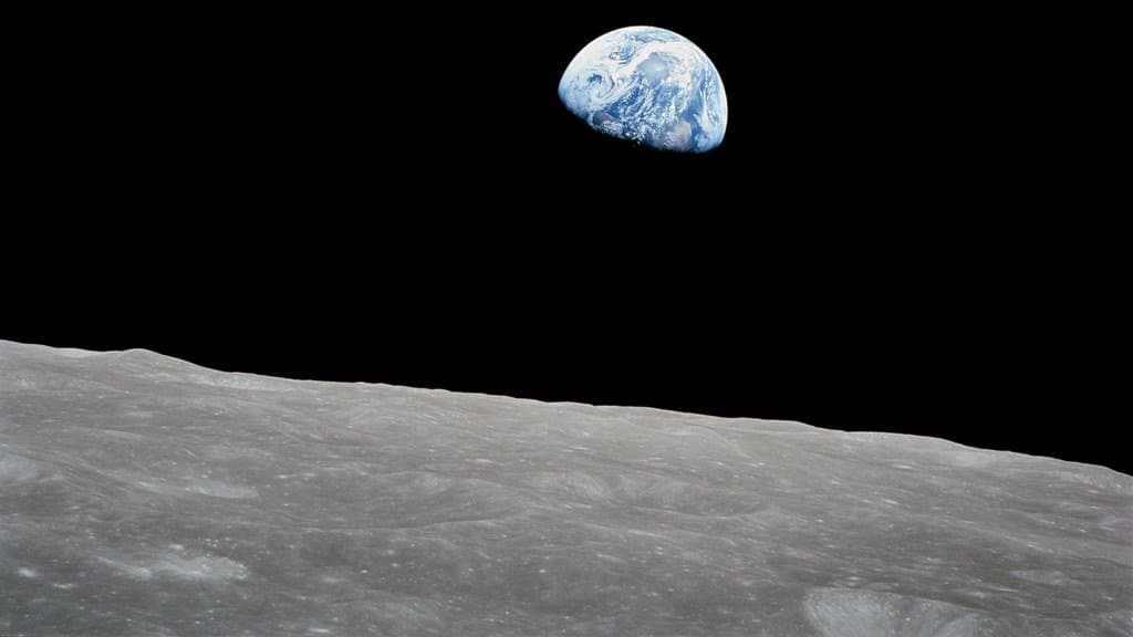 The blue and white disk of Earth, half in shadow, above the gray cratered surface of the Moon against black space.