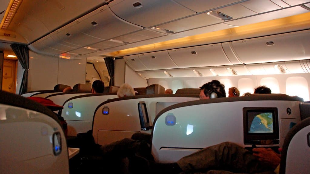 Rows of reclining business-class seats with seat-back screens inside a wide-body airliner cabin.