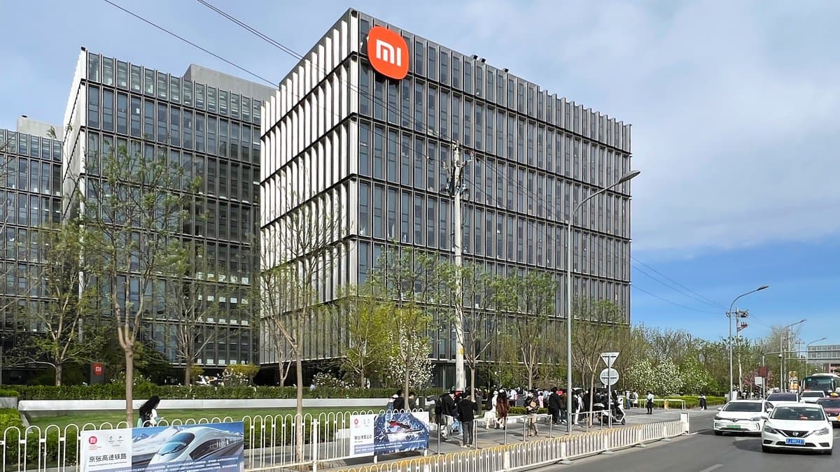 Office blocks of Xiaomi's Beijing headquarters campus under a blue sky, with a large orange Xiaomi logo mounted high on the corner of the nearest building.