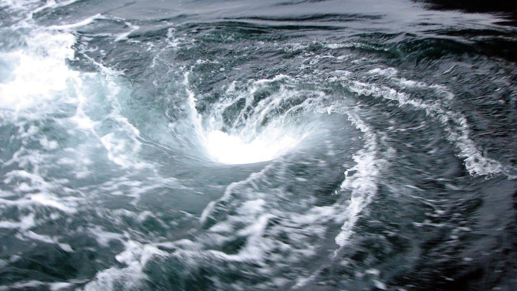 A whirlpool turning in dark green seawater, white foam spiraling into a bright center.