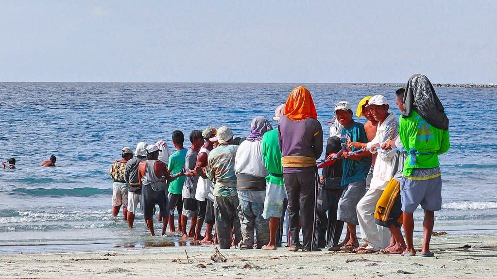 A line of people standing on a beach in the Philippines pull a fishing net in from the sea.