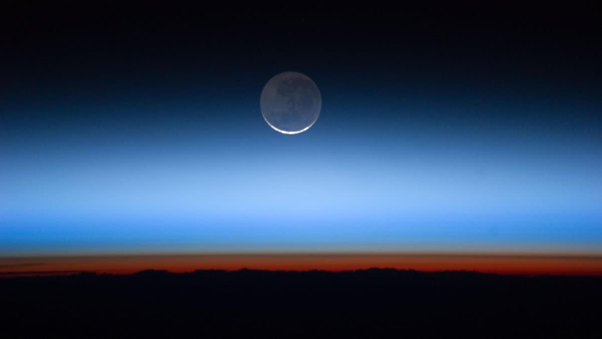 The Moon above Earth's horizon seen from orbit, the atmosphere below it separating into an orange band and a blue layer above