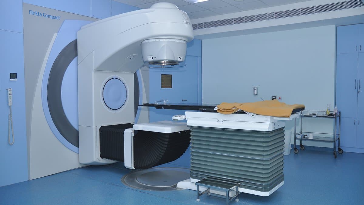An empty radiotherapy treatment room, with a linear accelerator positioned over a treatment couch.
