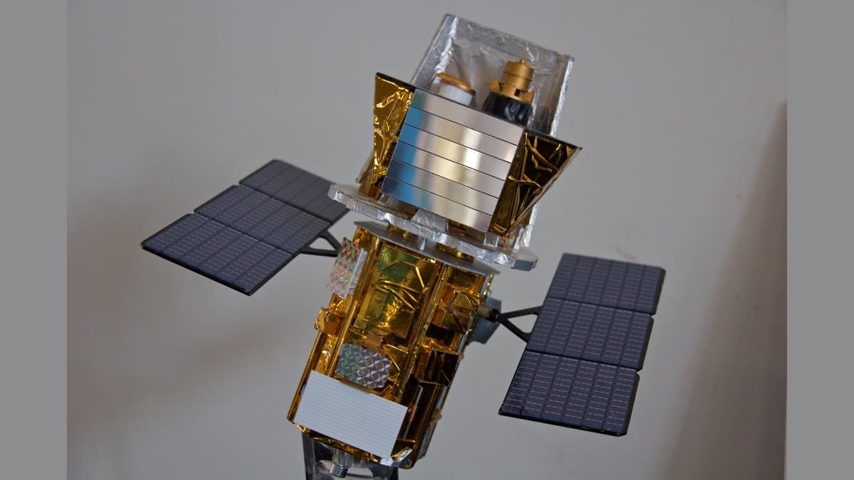A detailed scale model of NASA's Swift observatory, with a gold-foil-wrapped body, two dark solar panels angled out to the sides, and a boxy telescope assembly mounted on top.