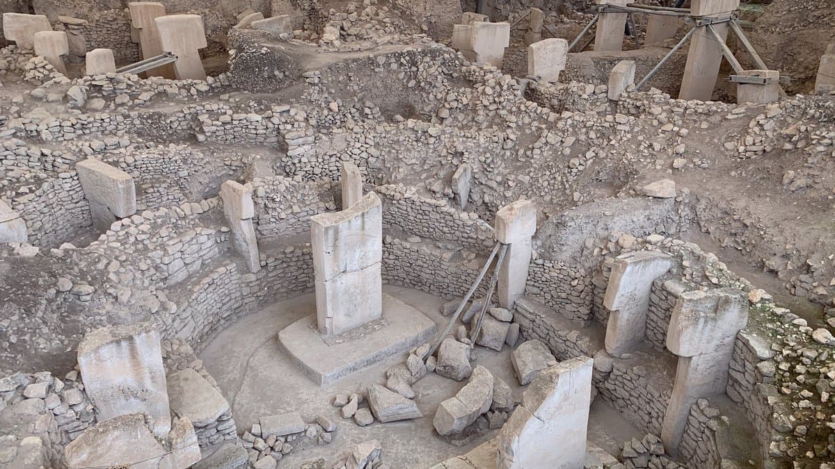Excavated circular stone enclosure at Gobeklitepe with two tall T-shaped limestone pillars standing at its center, ringed by dry-stone walls and open trenches.