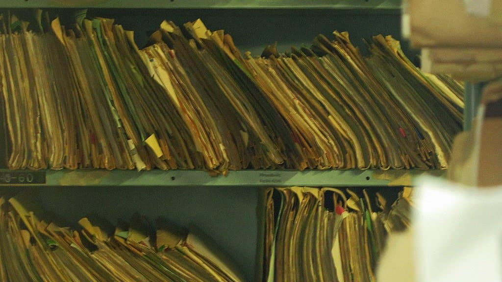 Shelves packed with bulging paper patient files in a medical records room