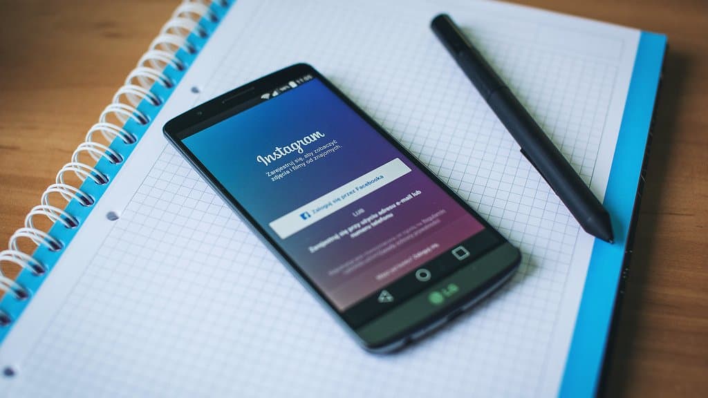 A smartphone resting on a spiral notebook beside a pen, its screen showing the Instagram sign-in page.