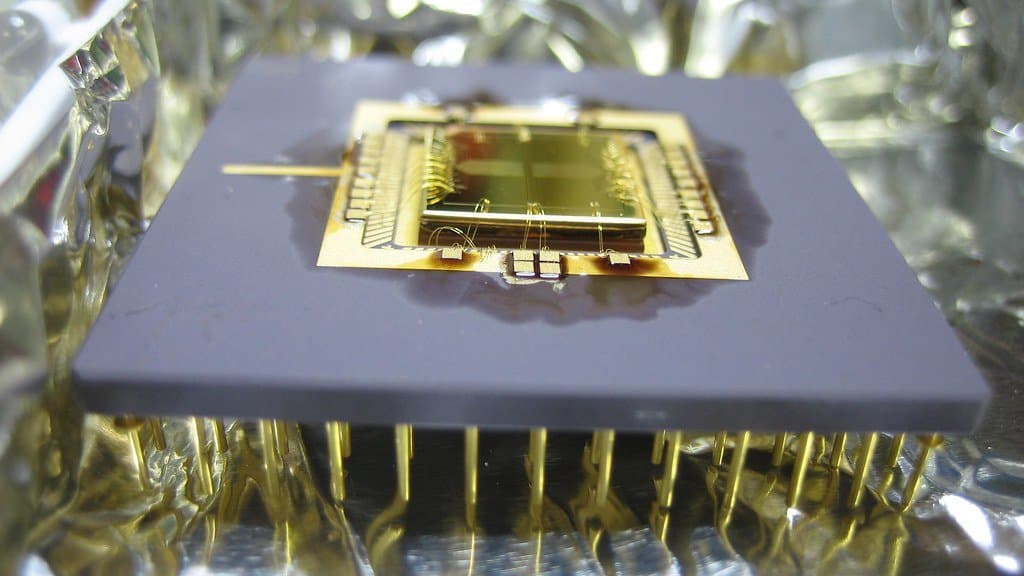 Macro photograph of a gold wire-bonded surface ion trap chip mounted on a ceramic carrier and resting on metal foil.