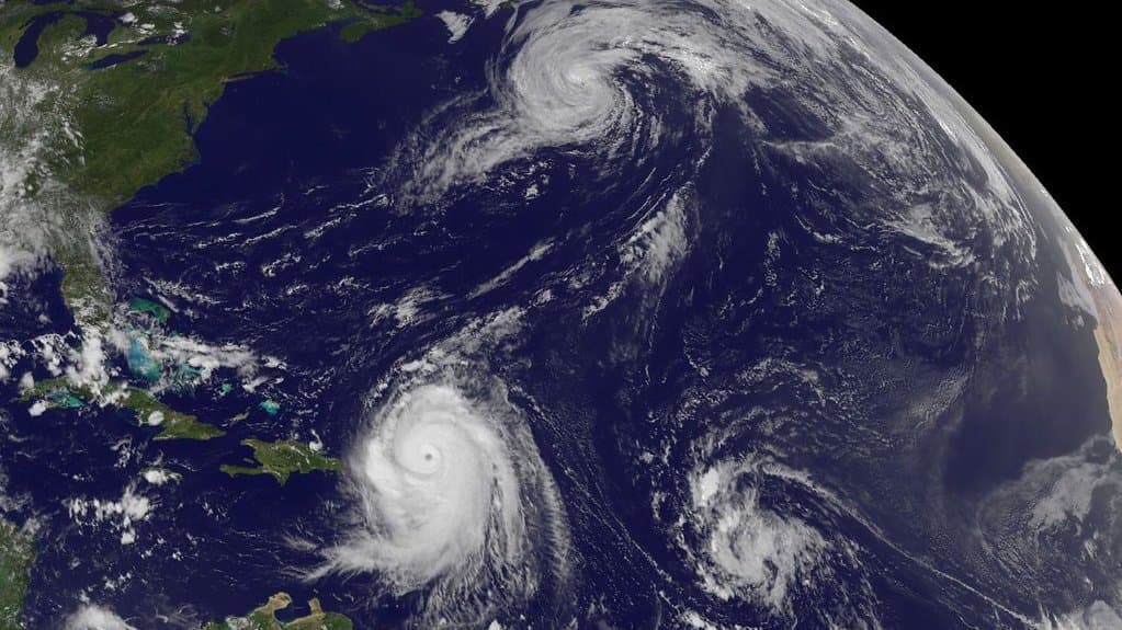 Satellite view of the western North Atlantic with three tropical cyclones turning at once, the eastern United States and the Caribbean islands visible at left.