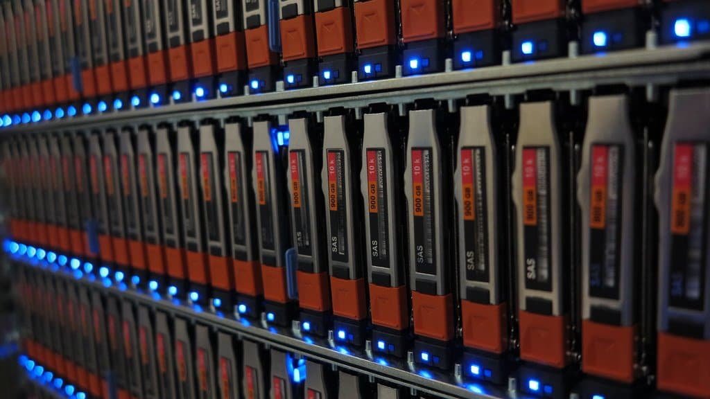 Close-up of rows of hot-swap disk drives in an enterprise storage array, with blue activity lights along each row.