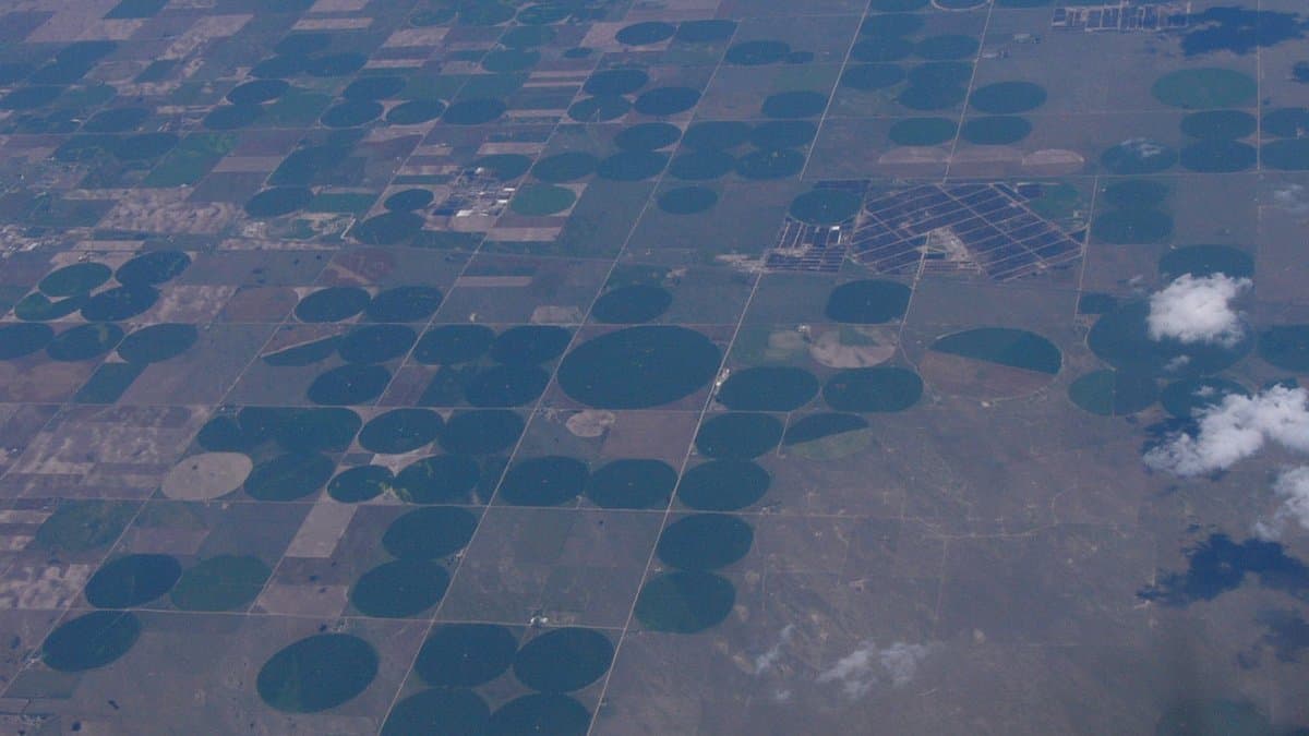 Aerial photograph of farmland in the western United States, with dark green circular irrigated fields scattered across pale brown dry ground.