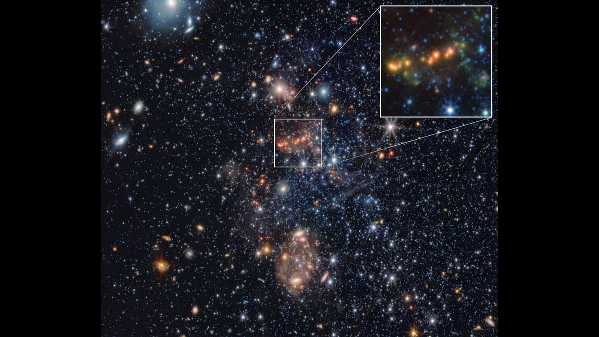 Infrared view of the dwarf galaxy Sextans A, a loose spread of blue and orange stars on a dark sky, with a white box marking a small region that is enlarged at upper right to show a chain of orange and green knots.