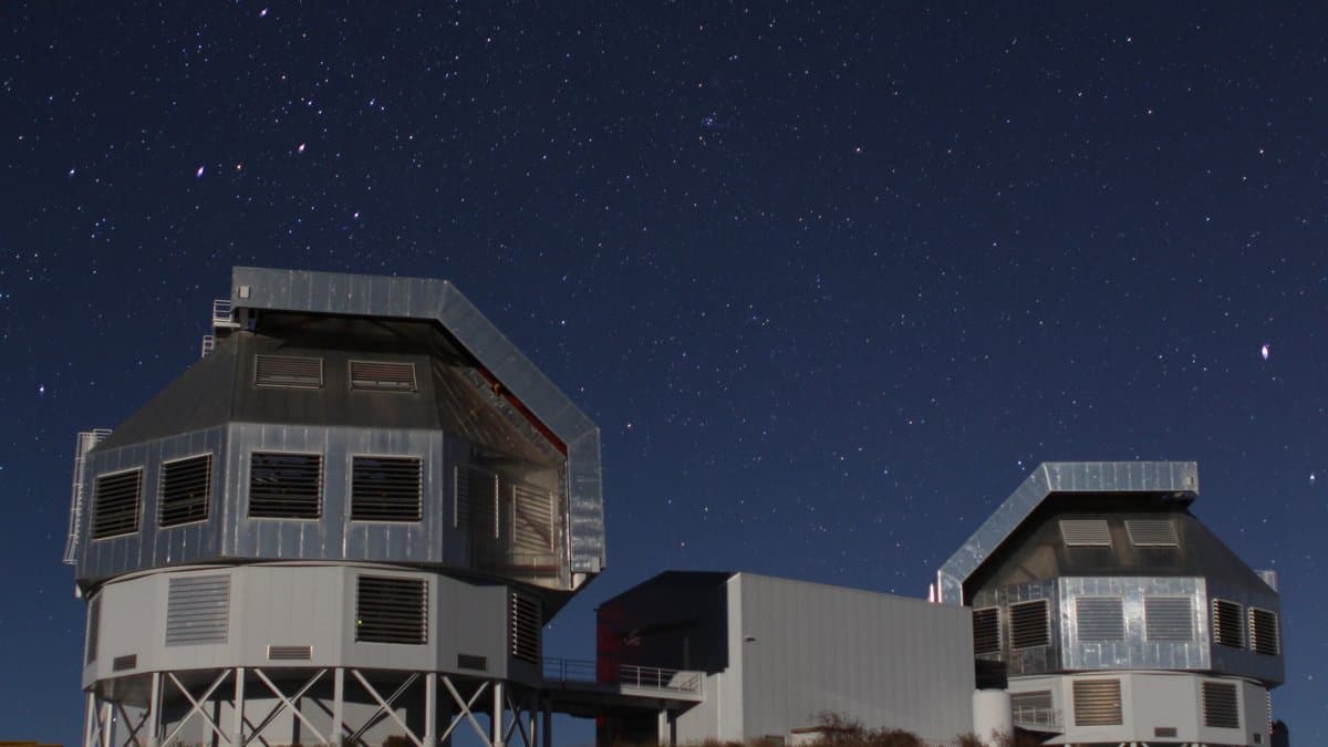 Two large silver telescope enclosures on a desert ridge under a star-filled night sky.