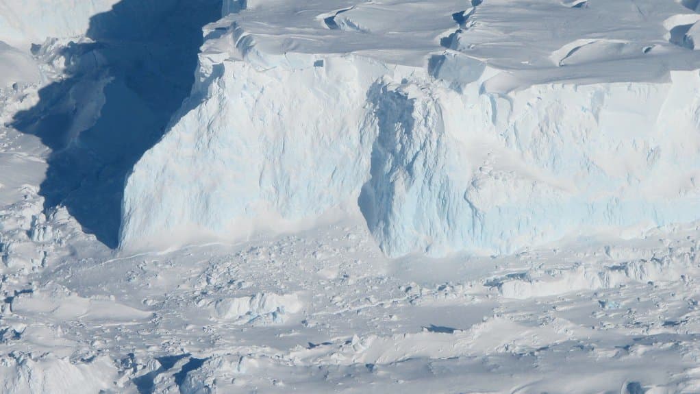 Aerial view of the tall ice cliff at the seaward front of Thwaites Glacier in West Antarctica, with broken ice rubble at its base.