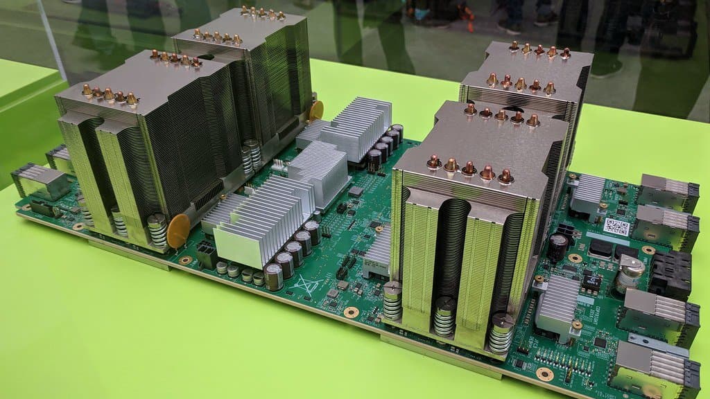 A green circuit board carrying four tall metal heatsinks and rows of capacitors, displayed on a green stand inside a glass case.