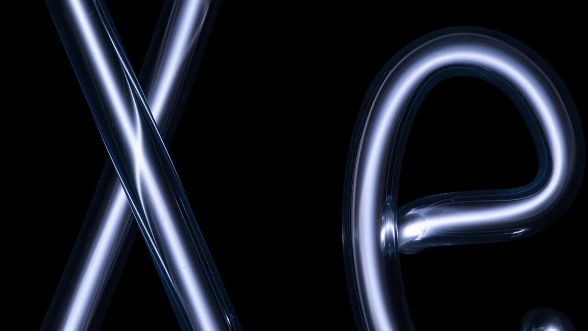 A glass discharge tube bent into the chemical symbol Xe, glowing pale blue-white with ionised xenon