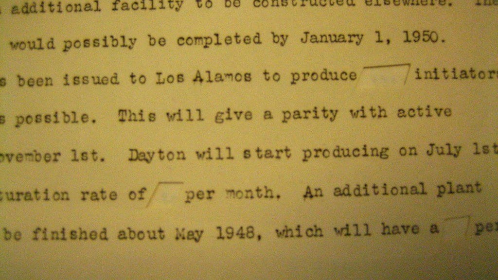 Close-up of a typewritten 1940s memorandum in which several words have been physically cut out of the paper, leaving blank slots in the middle of sentences about production schedules.
