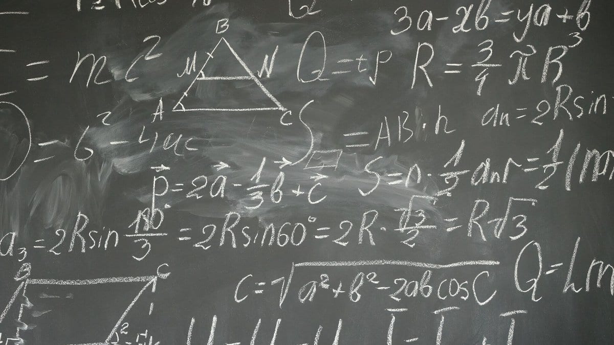 A blackboard densely covered with handwritten mathematical formulas and a labelled triangle, in white chalk.