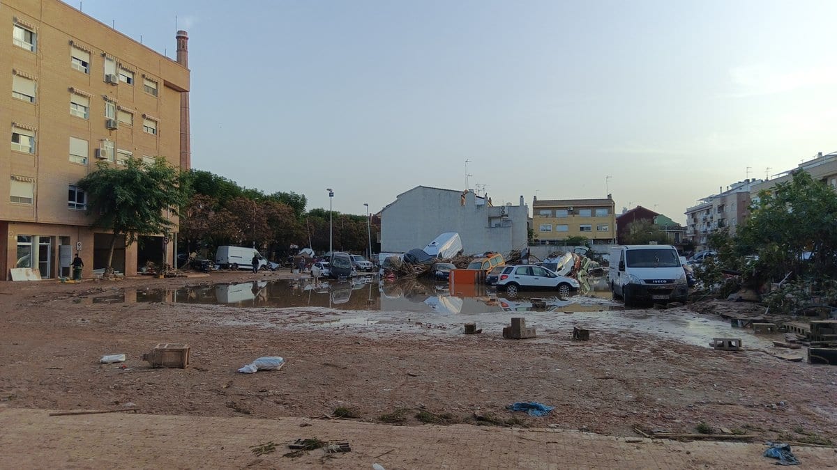A mud-covered street in Paiporta near Valencia the day after the October 2024 flash flood, with cars shoved into piles, standing brown water and debris across the roadway