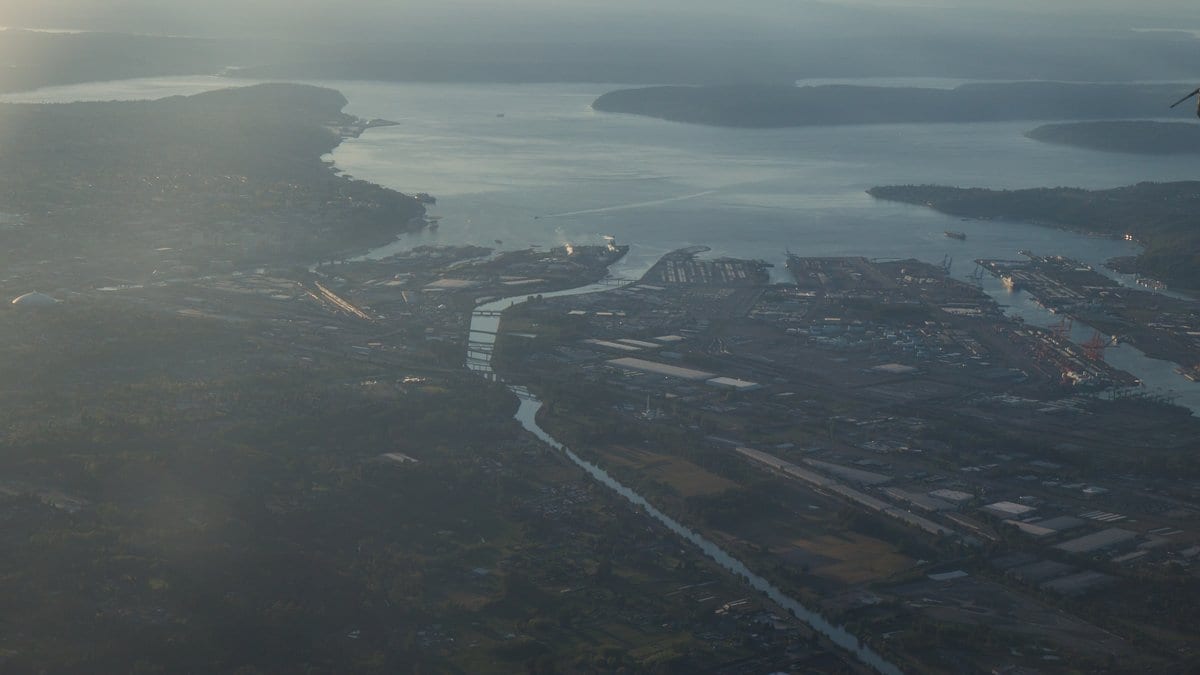 Elevated aerial view across downtown Tacoma and the low-lying Commencement Bay tide flats, with the Puyallup River channel and port terminals meeting the water of Puget Sound