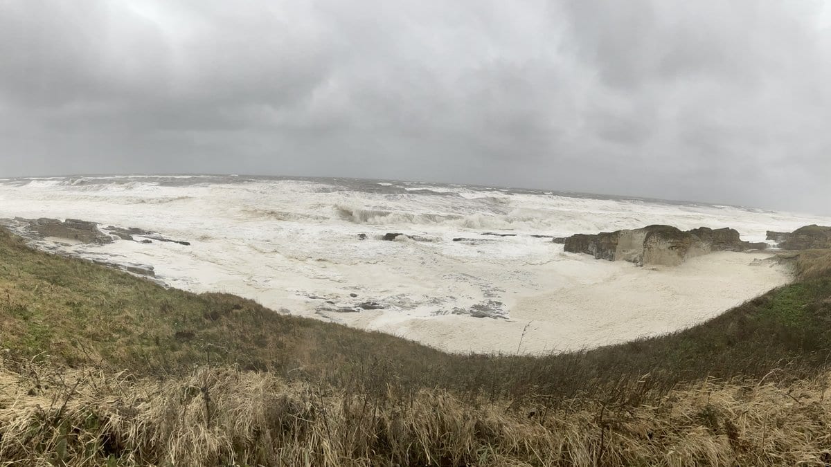 Storm waves and thick foam filling a rocky cove under a heavy grey sky on the Northumberland coast