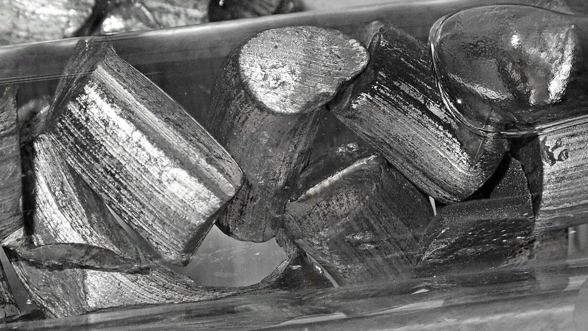 Cut chunks of silvery lithium metal with bright, striated freshly exposed surfaces, stored under oil.
