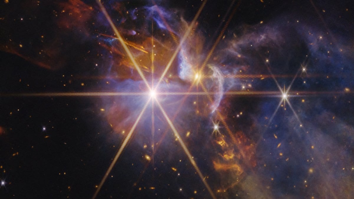 A James Webb Space Telescope near-infrared image of the young star system FS Tau: a brilliant star with long diffraction spikes, surrounded by orange and blue clouds of gas and dust and a curved outflow arc.