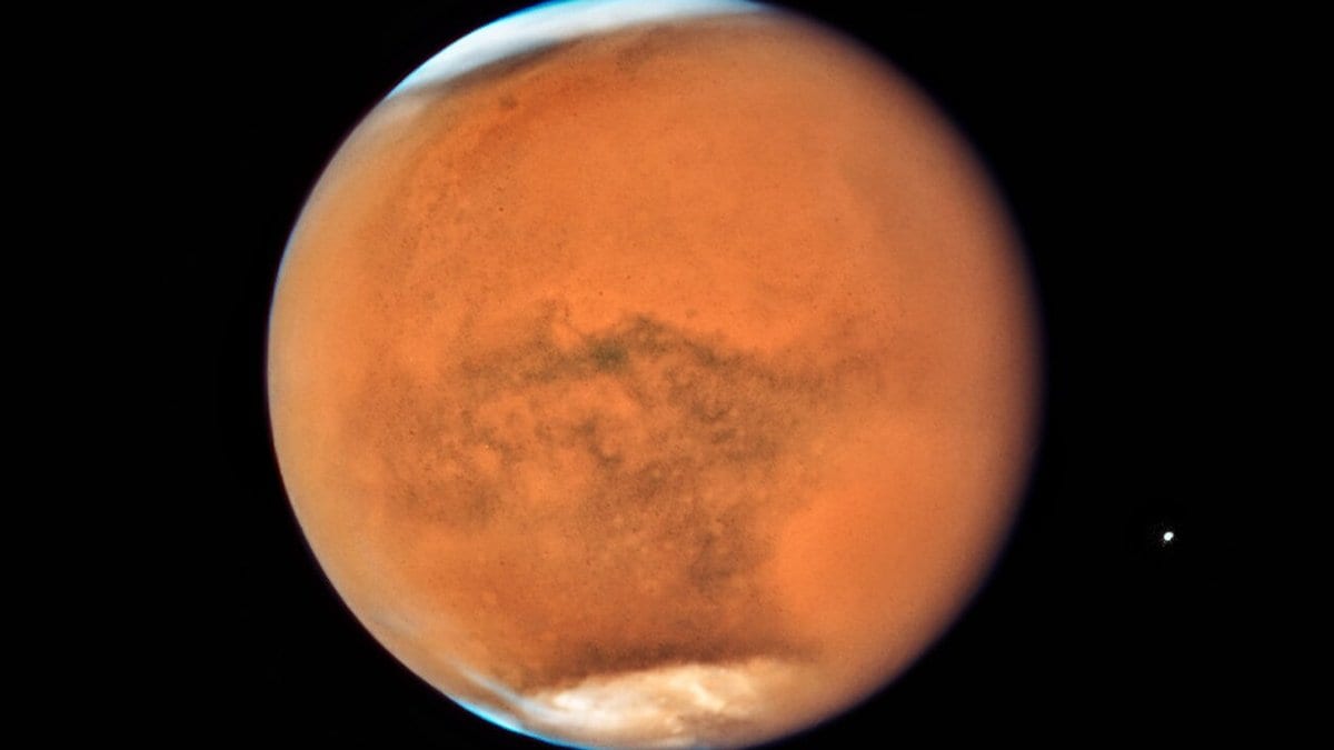 Full disc of Mars seen from space, its surface veiled in orange dust during the 2018 planet-encircling dust storm, with a bright white south polar cap and a thin blue haze along the limb.