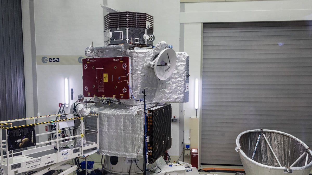 The assembled BepiColombo spacecraft stack in an ESA clean room: the silver Mercury Transfer Module at the bottom, mounted on a cone-shaped adapter; the Mercury Planetary Orbiter, with a dark red cover panel, in the middle; and JAXA's Mercury Magnetospheric Orbiter on top, with an engineer in a white clean-room suit working alongside
