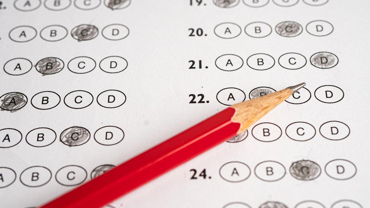 Close-up of a multiple-choice answer sheet with several bubbles filled in and a sharpened red pencil lying across it