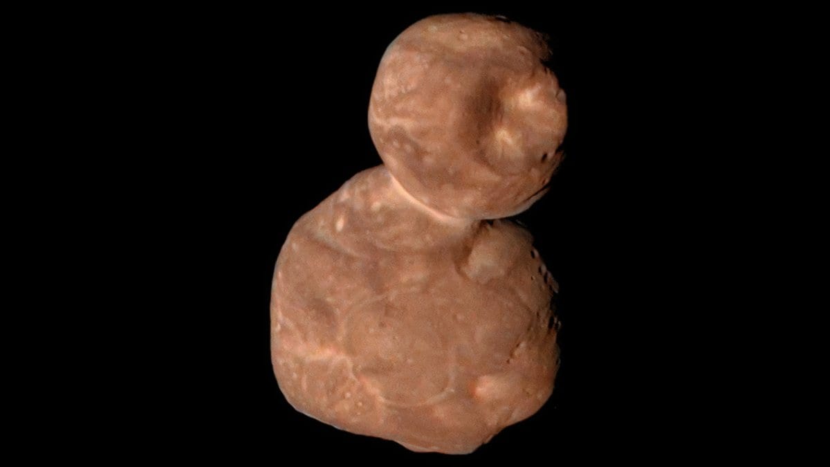 The two-lobed, reddish icy body Arrokoth against black space, a small round lobe joined to a larger flattened one, its surface mottled with bright patches and shallow pits.