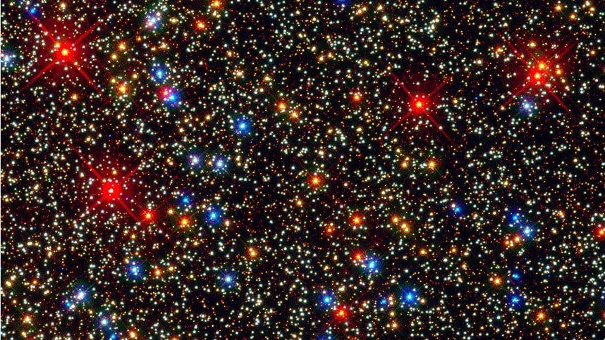 A dense field of thousands of stars in the globular cluster Omega Centauri, with several bright red stars among blue and white ones.