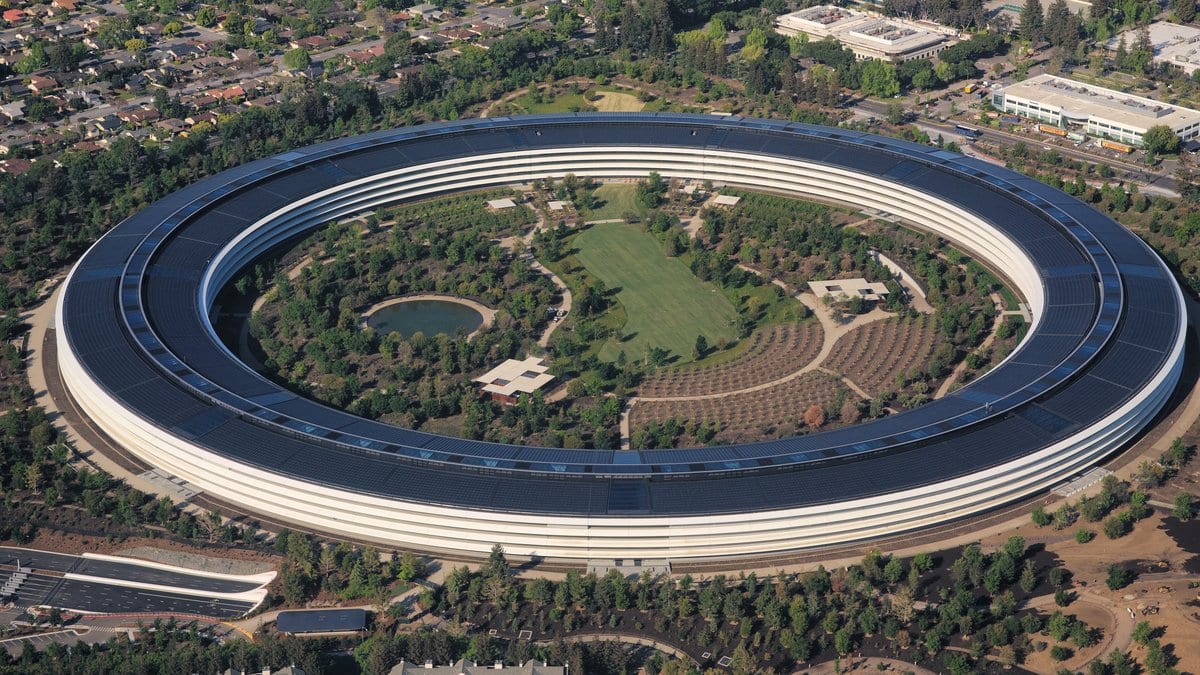 Aerial view of Apple Park in Cupertino, California, a large ring-shaped building with a solar-panel roof enclosing a landscaped courtyard.