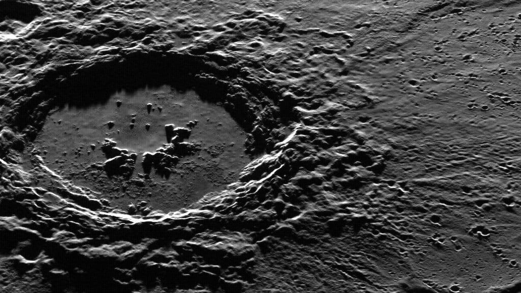 Spacecraft image of Mercury showing a large impact crater with a rugged rim and hummocky floor, surrounded by cratered plains crossed by low ridges.