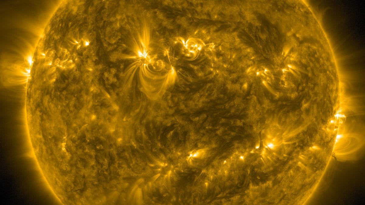 The full disk of the Sun imaged in extreme ultraviolet light, with bright active regions and arcs of plasma over a mottled surface.